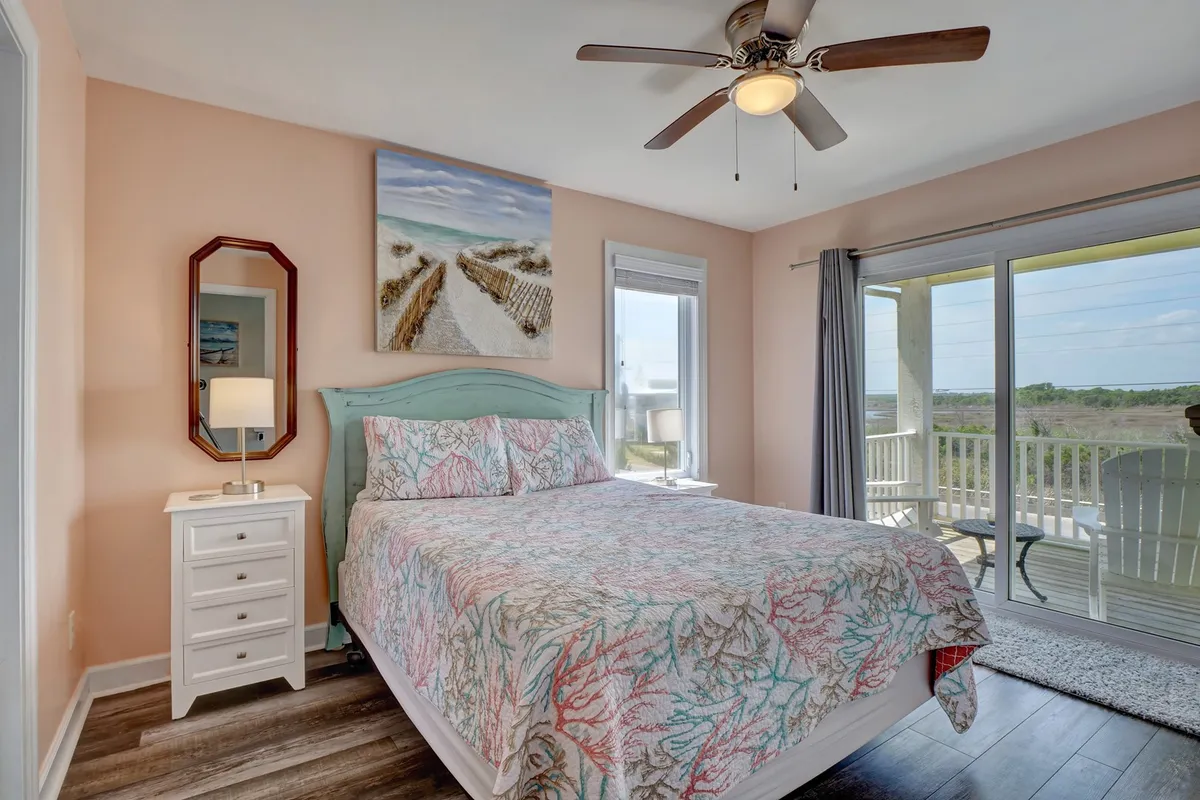 A tranquil bedroom featuring a bed with colorful bedding, large window with a scenic view, and calming accents like a nightstand with lamp and artwork. Soft natural light fills the space, creating a restful and customizable retreat.
