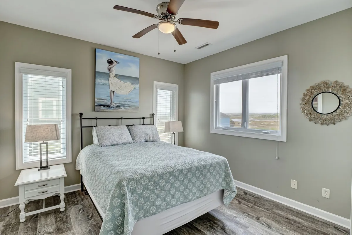 A queen bedroom featuring a comfortable bed, calming artwork, a window with a view, and soft lighting from bedside lamps. The room exudes tranquility and is conveniently located near the central living spaces.