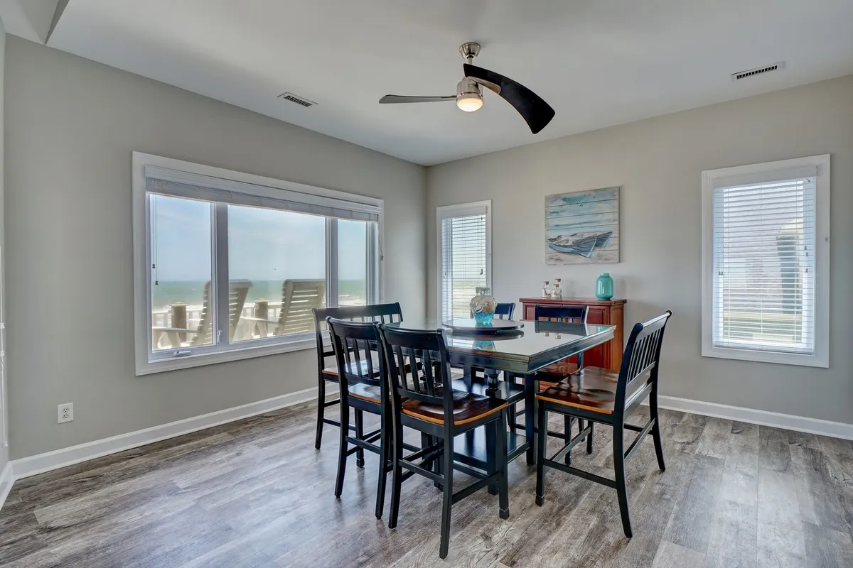 A dining area with a large wooden table that seats eight, positioned near expansive windows that bathe the room in natural light. Decorative wall art and comfortable chairs add to the homey, communal feel—perfect for family feasts or game nights.