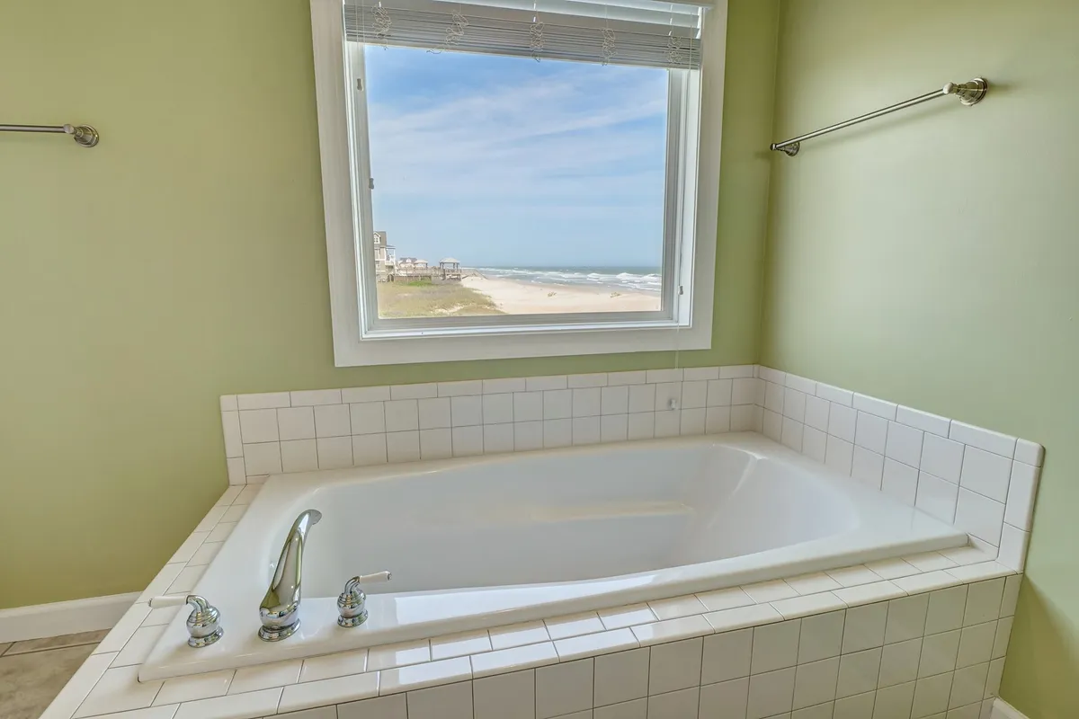 A calming bathroom scene with a sleek bathtub positioned near a window that frames a peaceful view. The space invites relaxation, with clean lines and soft light creating a spa-like setting.