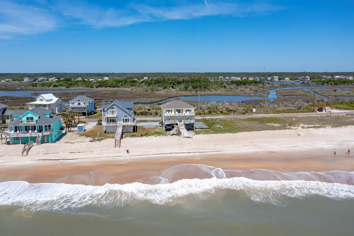 An inviting beachfront scene with gentle ocean waves, scattered beach houses, and marshland in the distance. The soft morning light hints at the start of a new day, ideal for sunrise watching, exploring nature trails, and observing local wildlife.
