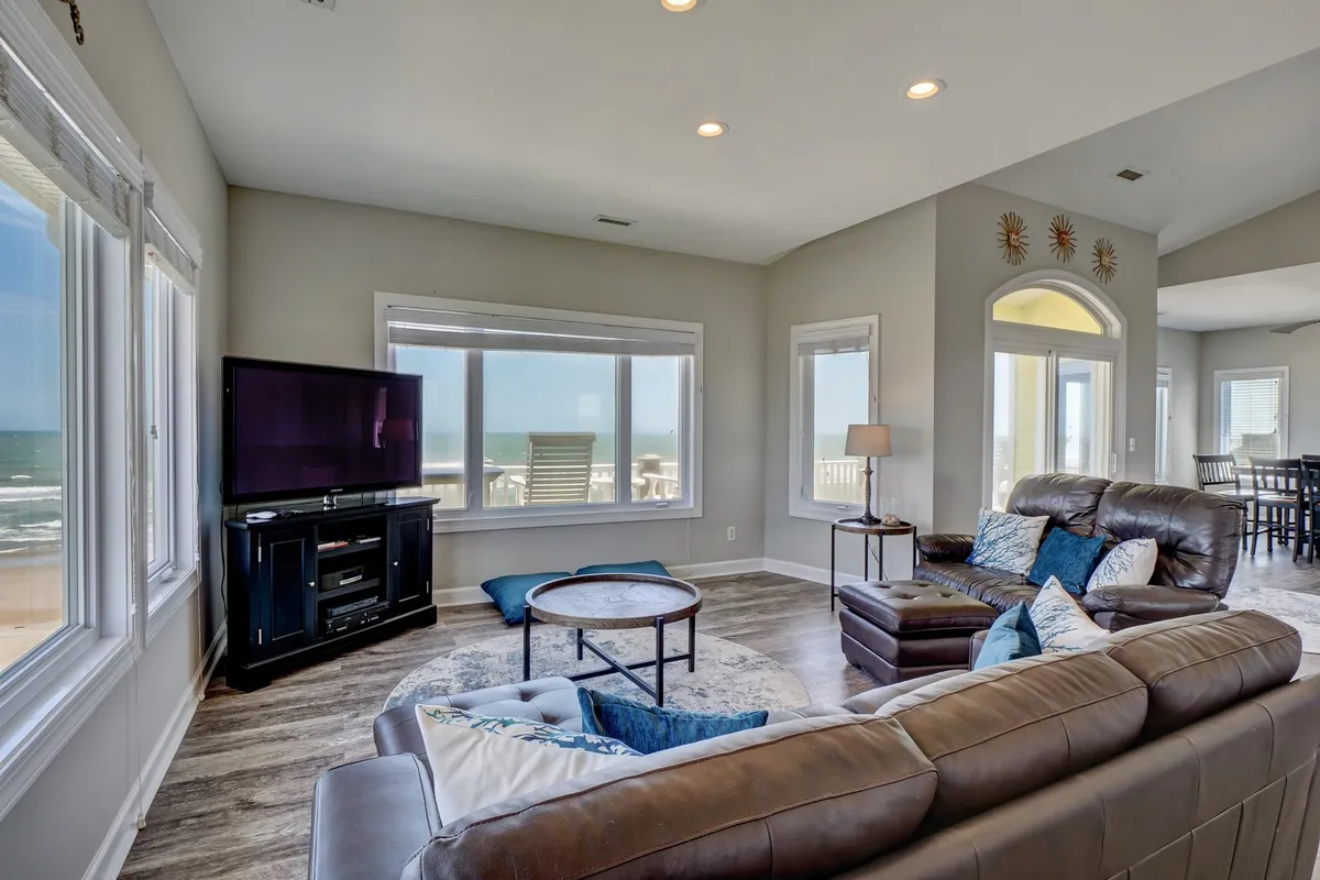 A spacious, light-filled living area with large windows offering ocean views, a comfortable seating arrangement, and a TV unit. The décor feels casual yet welcoming, ideal for relaxing, watching movies, or socializing with friends and family.